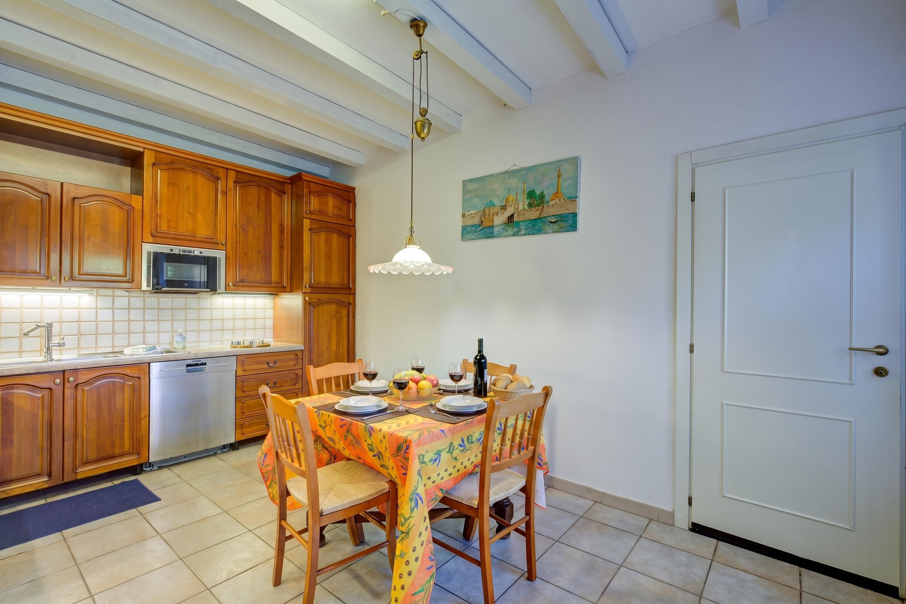 Una cocina con armarios de madera, microondas y una mesa de comedor preparada para cuatro personas con sillas.