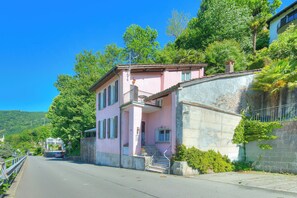 A pink building with a balcony, a staircase, and a road in the background. - Villa Lake View With BBQ (Lugano)