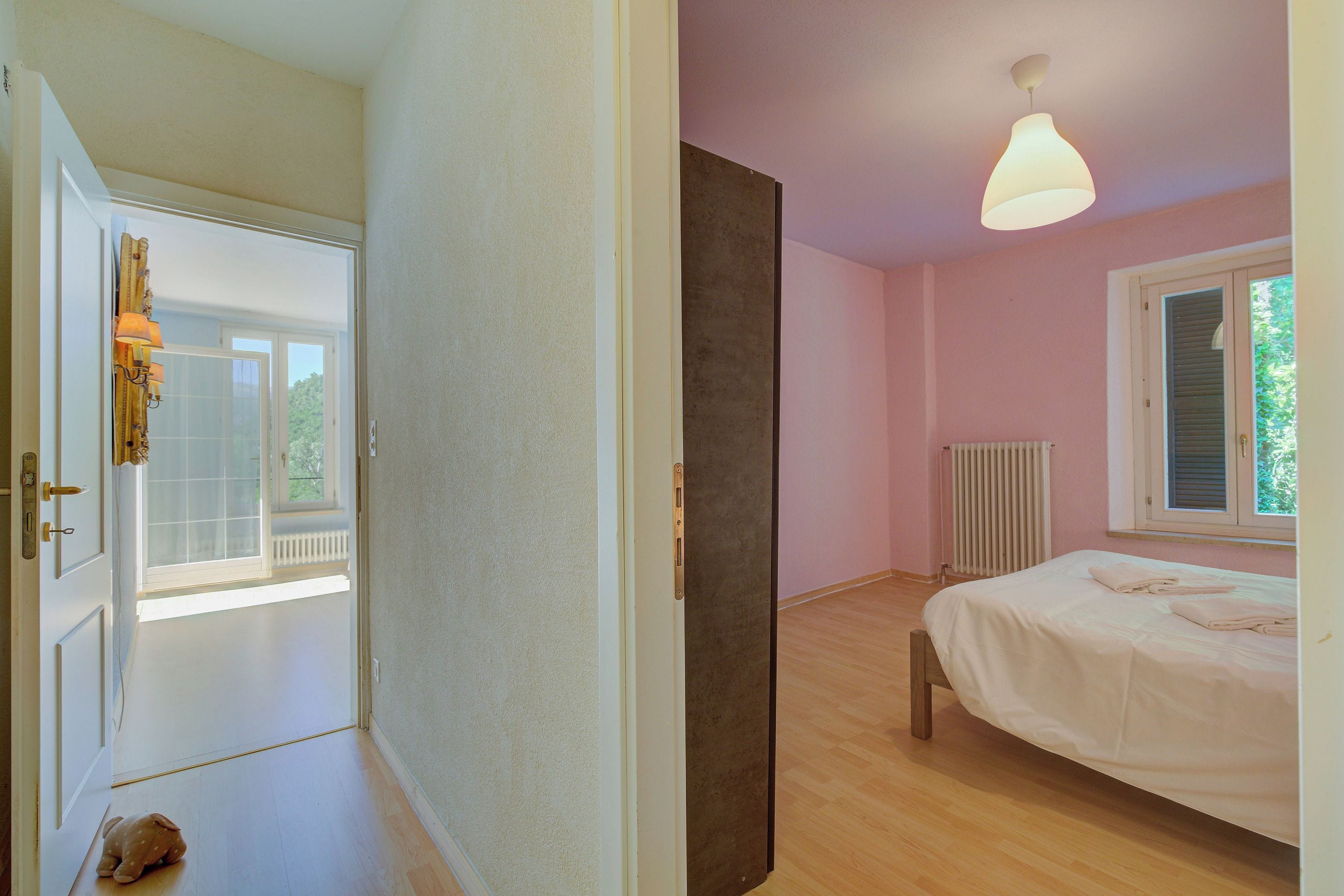 A bedroom with a bed, a window, a radiator, and a door leading to another room.