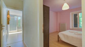 A bedroom with a bed, a window, a radiator, and a door leading to another room.