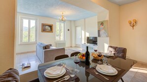 Un coin repas avec une table dressée pour deux personnes, un lustre et un tableau accroché au mur.