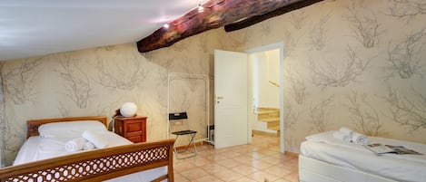 Une chambre avec un lit en bois, un canapé blanc, une petite table et une chaise. Un escalier mène à une autre pièce.