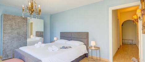 A bedroom with a large bed, bedside lamps, a mirror, and a chandelier.