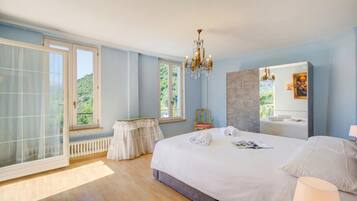 A bedroom with a large bed, a chandelier, a window with a view, a radiator, and a small table.