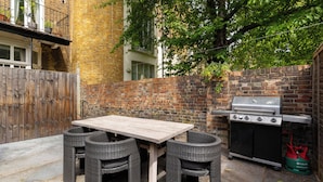 A patio with a table and chairs, a grill, and a gas tank. - Brass & Shaker Clapham (London)