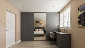 A bedroom with a bed, a desk, and a chair. There is a wardrobe and a window with blinds. - Brass & Shaker Clapham (London)