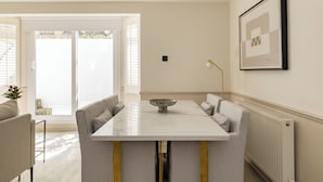 A dining area with a white table, striped chairs, a bowl centerpiece, and a framed picture on the wall. - Brass & Shaker Clapham (London)