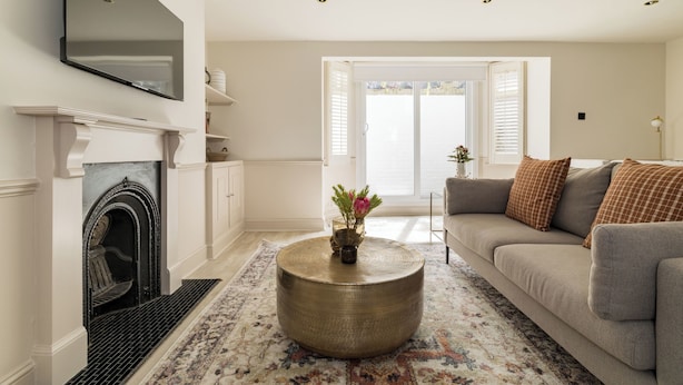 A living room with a fireplace, a round coffee table, a sofa, and a television mounted on the wall. - Brass & Shaker Clapham (London)