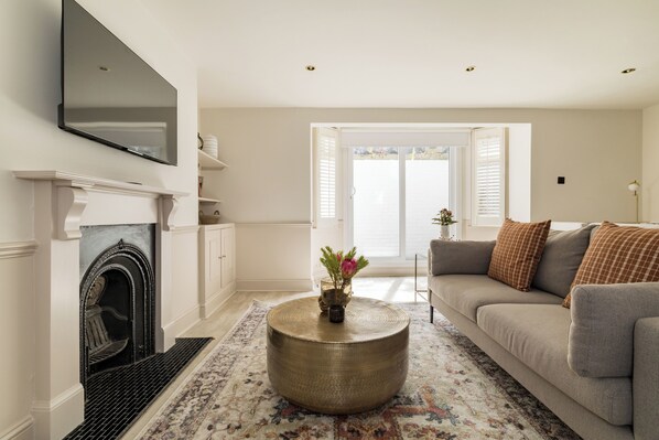 A living room with a fireplace, a round coffee table, a sofa, and a television mounted on the wall. - Brass & Shaker Clapham (London)