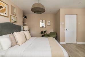 Een slaapkamer met een bed, hoofdbord, lamp, deur en decoratieve wandkunst.