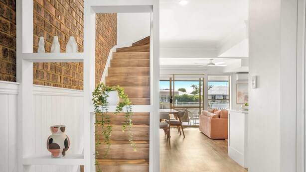 Un interior moderno con escalera de madera, paredes blancas y vistas al exterior.
