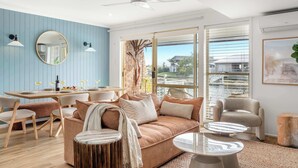 Una sala de estar moderna con un sofá, sillas, una mesa de comedor y un ventanal con persianas.