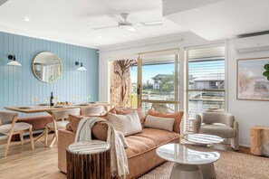 Ein modernes Wohnzimmer mit einer Couch, Sesseln, einem Esstisch und einem großen Fenster mit Jalousien.