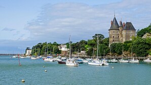 Un paysage côtier avec un château historique, une marina où sont amarrés différents bateaux et une végétation luxuriante.