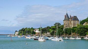 Un paysage côtier avec un château historique, une marina où sont amarrés différents bateaux et une végétation luxuriante.