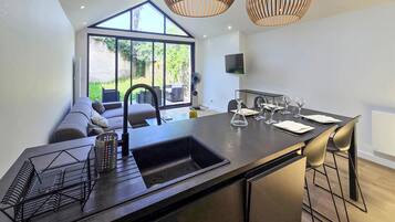Une cuisine moderne dotée d’un grand îlot central, de tabourets de bar, d’un four encastré et d’une grande fenêtre donnant sur un jardin.