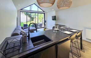 Une cuisine moderne dotée d’un grand îlot central, de tabourets de bar, d’un four encastré et d’une grande fenêtre donnant sur un jardin.