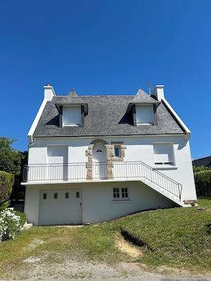 Una casa de dues plantes amb un balcó, entrada de pedra i teulat inclinat.
