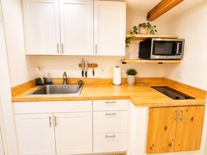 A kitchen with white cabinets, wooden countertops, a sink, a microwave, and a potted plant. - Cedar and Stone Studio (San Diego)