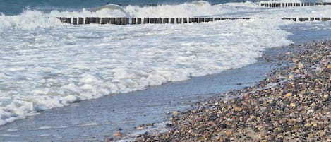 A pebble beach with waves crashing onto the shore and a wooden pier extending into the water.