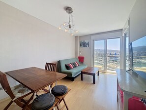 Ein modernes Wohnzimmer mit Esstisch, einer Couch und Blick auf eine Stadtlandschaft durch große Fenster.