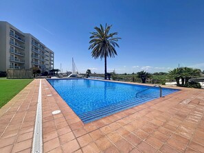 Ein Pool mit gefliestem Sonnendeck, einer Palme und einem Gebäude im Hintergrund.