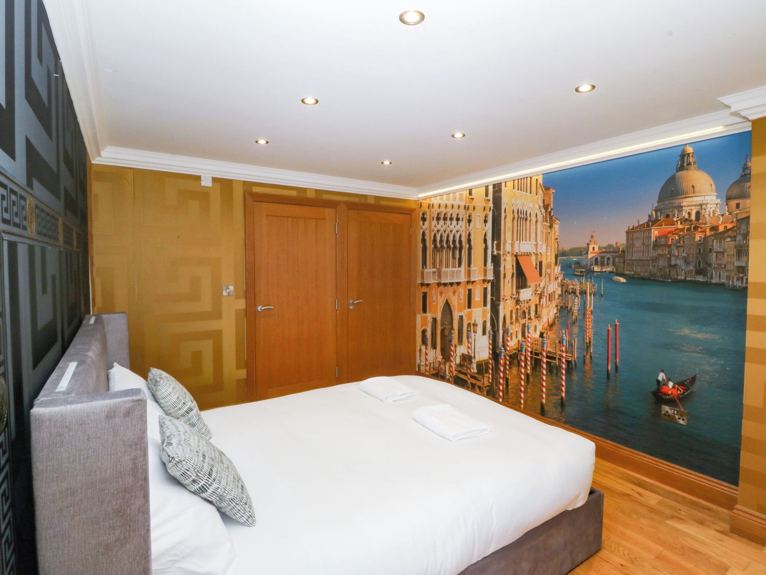 Een hotelkamer met een groot bed, een houten kledingkast en een muurschildering van het Canal Grande in Venetië.