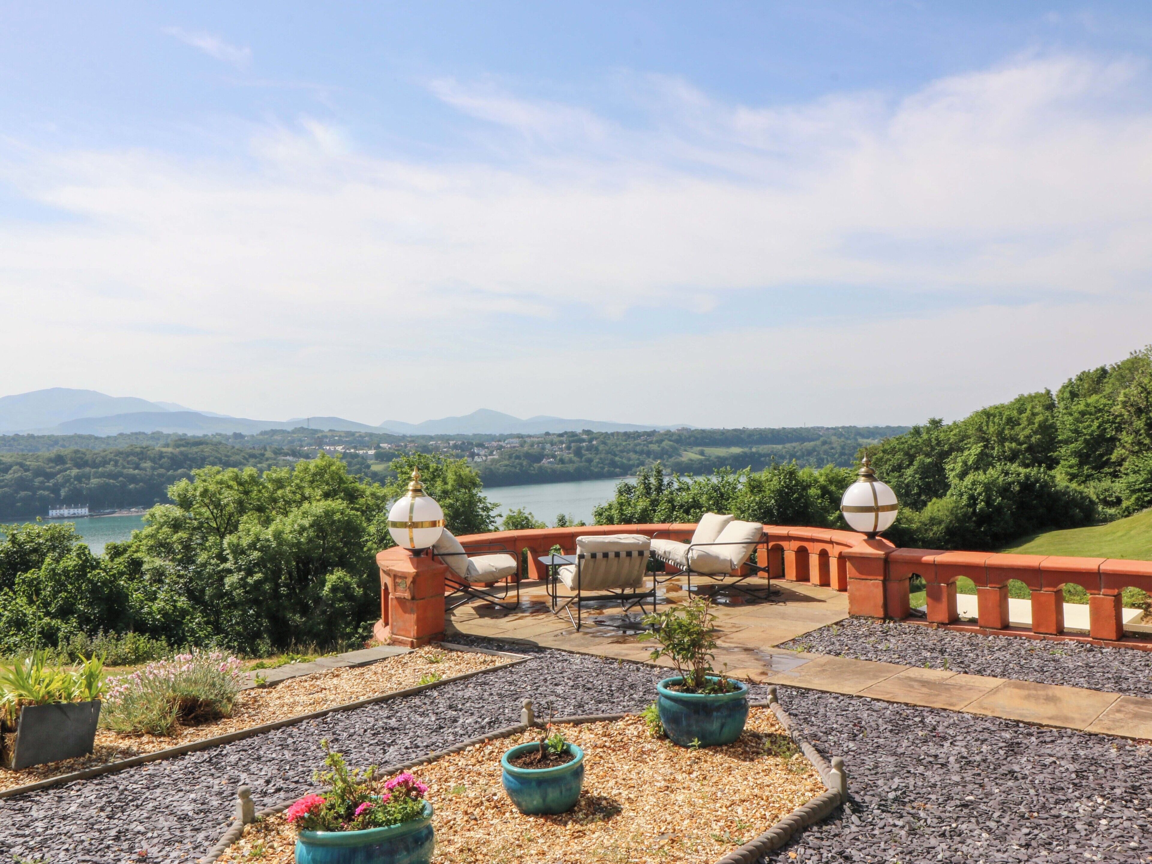 Un patio con mobiliario exterior, plantas en macetas y una vista panorámica de un lago y montañas.