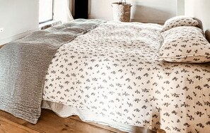 Ein Bett mit einer blumigen Tagesdecke, einer grauen Decke und einem gewebten Korb.