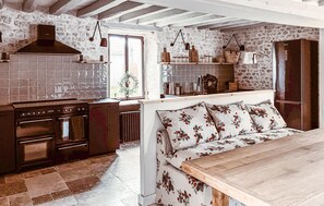 Eine Küche mit Herd, Backofen und Hängeleuchten; eine Bank mit Blumenkissen; und eine Steinwand.