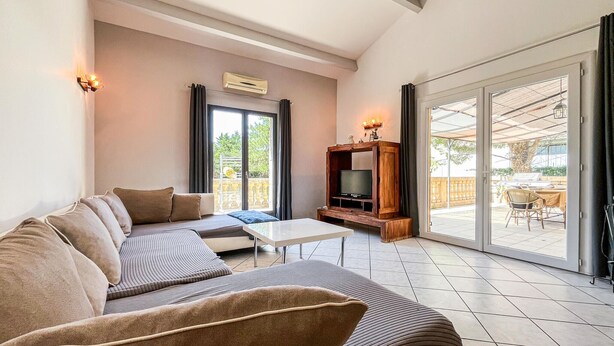 Een woonkamer met een bank, televisie en een schuifdeur naar een terras.
