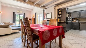 Een eetgedeelte met een rode tafelkleed, houten stoelen en een keuken op de achtergrond.