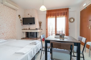 A hotel room with a bed, a small table with chairs, a fireplace, a television, and a window with curtains. - Konstantina`s House by Rentals Pro - Afytos Halkidiki (Afytos)