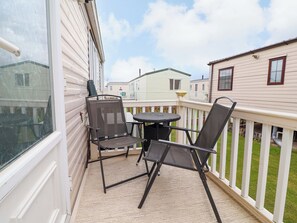 Ein Balkon mit zwei Stühlen und einem kleinen Tisch, weißen Geländern und Blick auf angrenzende Mobilheime.