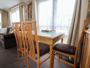 A room with a wooden dining table, two chairs, a sofa, and a decorative wall piece. - Winchester - 478 (Abergele)