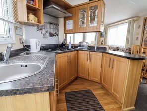 Eine Küche mit Holzschränken, einer Granit Arbeitsplatte, einer Edelstahl-Spüle, einem Herd und einem Fenster mit Vorhängen.