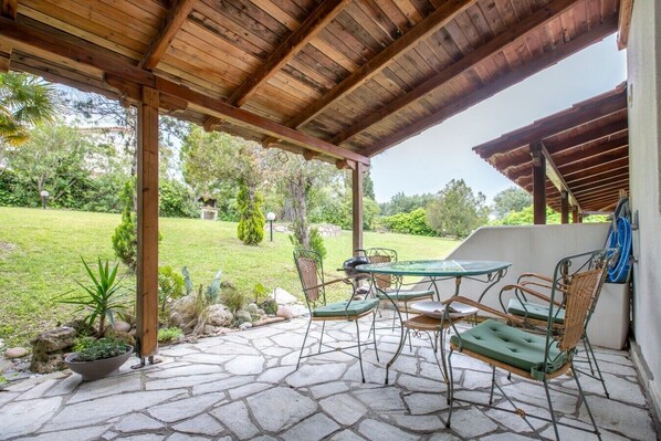 A covered patio with stone flooring, outdoor furniture, and a view of a grassy area.