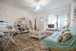 Un salon avec un sol en pierre, une étagère ronde blanche, un téléviseur et un canapé bleu clair.