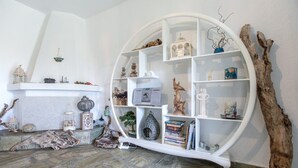 A room with a white circular shelving unit against a white wall, containing various decorative items and books. - Possidi Zen Maisonette by RentalsPro (Kassandreia)