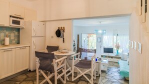 A compact kitchen with a dining area, a TV, and a view through an open door. - Possidi Zen Maisonette by RentalsPro (Kassandreia)