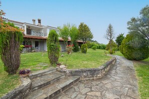 A stone pathway leading to a building with a tiled roof, surrounded by well-maintained grass and various shrubs.