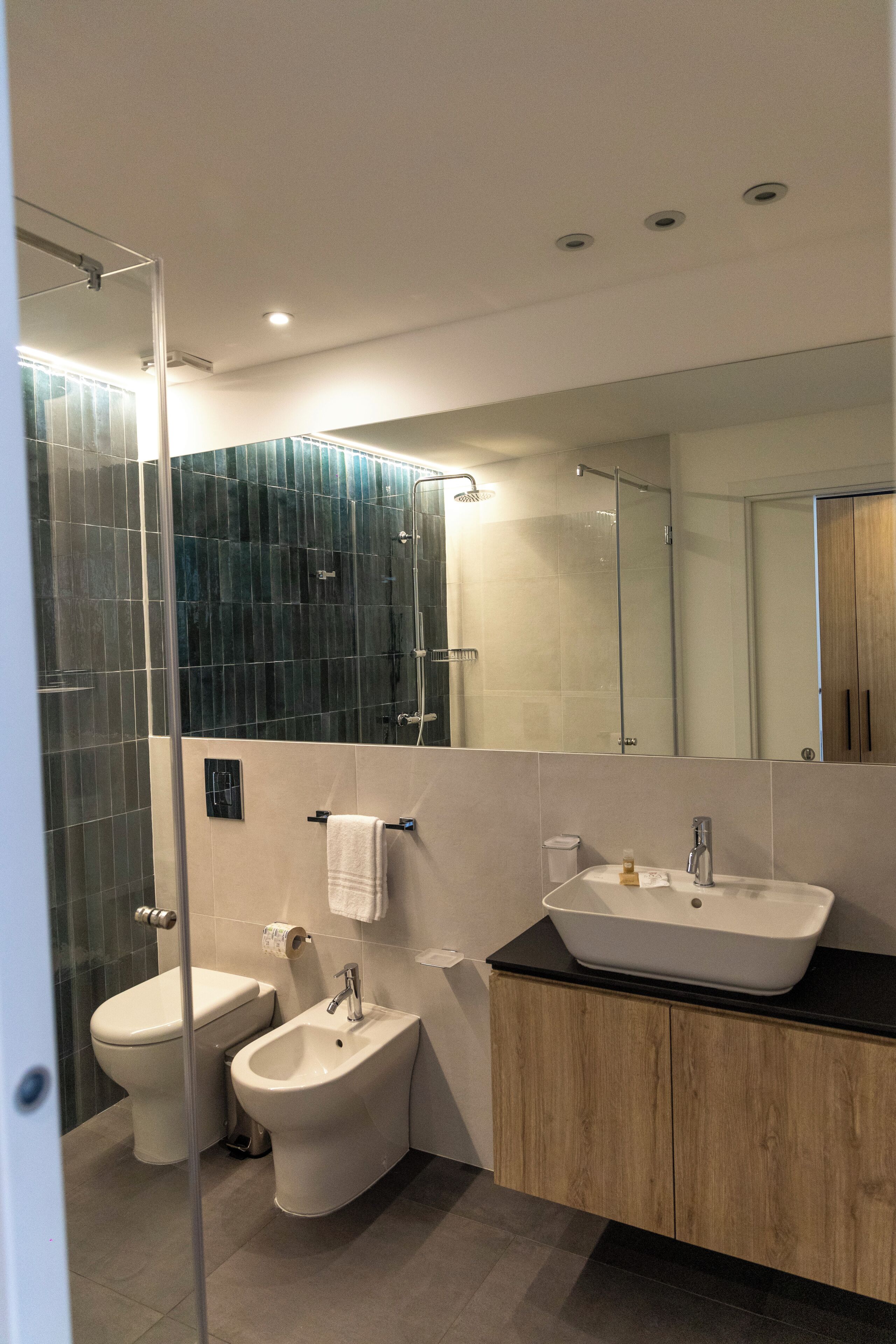 Ein modernes Badezimmer mit Duschkabine aus Glas, einem Bidet, einer Toilette und einem Waschbecken mit Spiegel darüber.