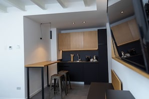 A modern kitchen with a wooden countertop, black cabinets, and a built-in oven. There are two stools and a small table.