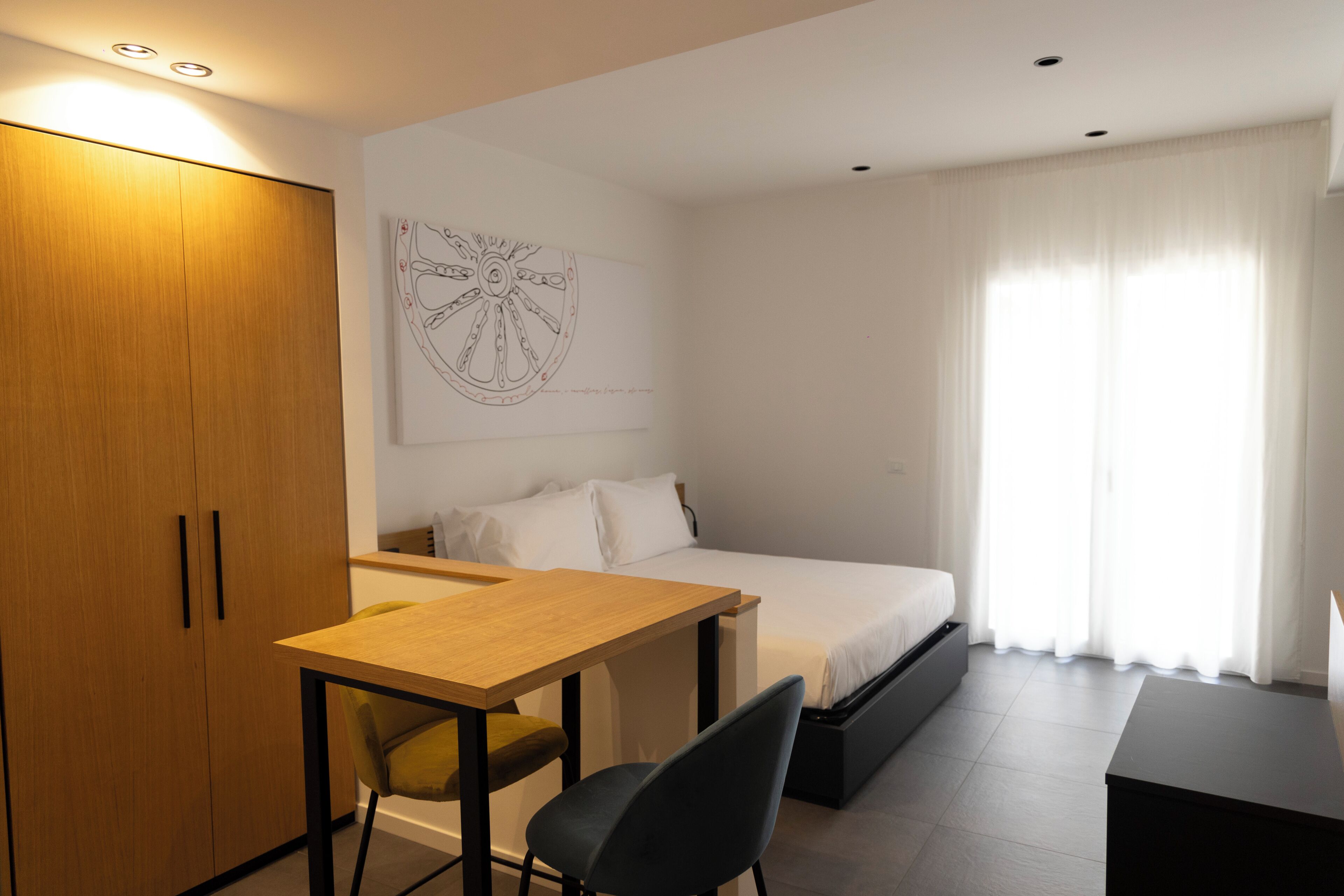 A bedroom with a bed, a desk, a chair, a wardrobe, and a window with curtains.