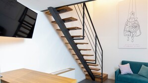 A modern interior with a wooden staircase, a teal sofa, and a flat-screen TV mounted on a wall. - La Dimora Dei Paladini (Bagheria)