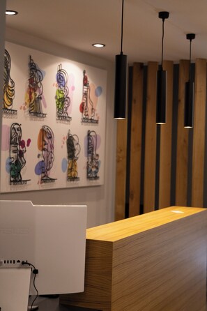 A reception desk with a wooden finish, a wall with abstract art, and pendant lighting.