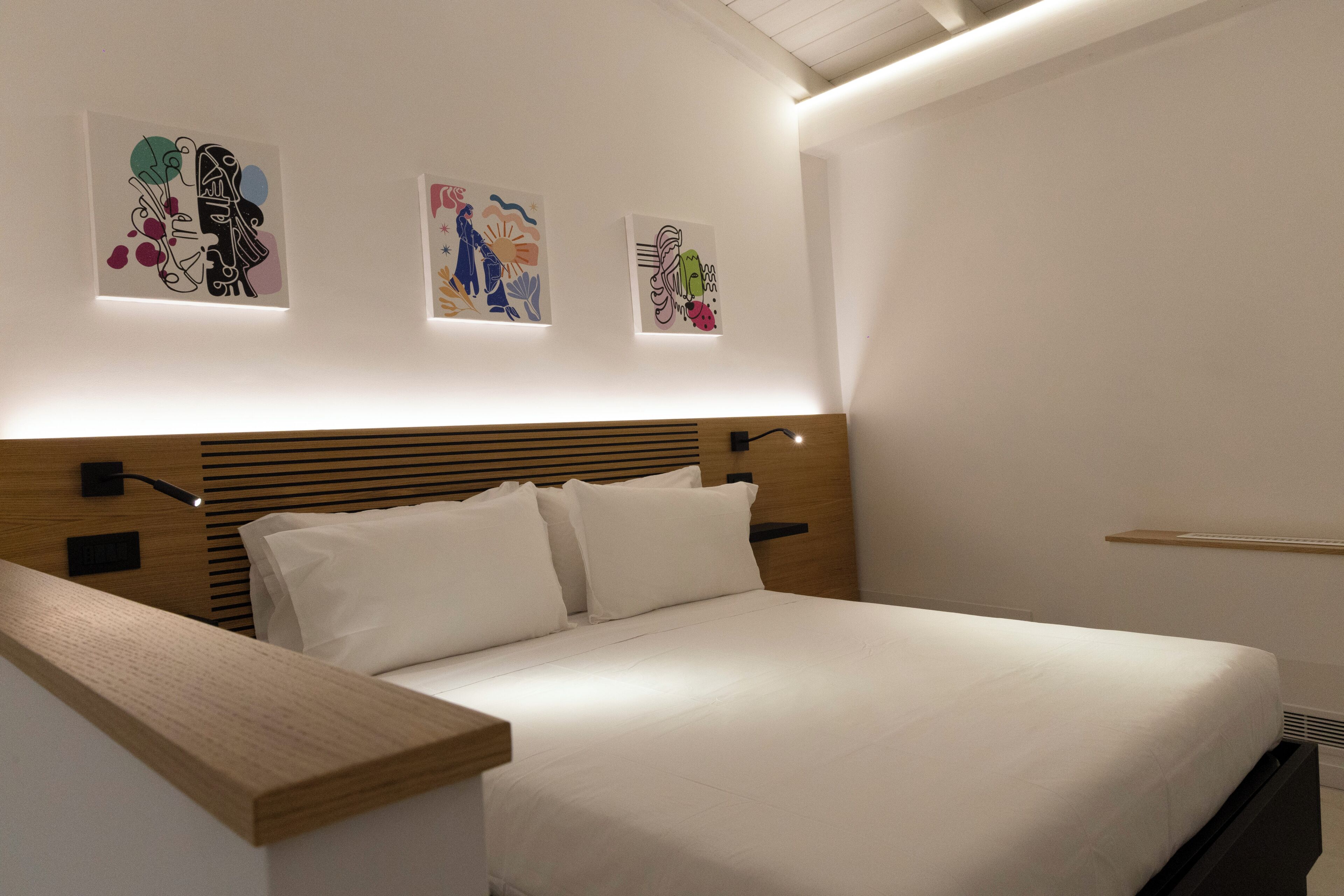 A modern bedroom with a wooden headboard, a white bed, and three abstract wall art pieces.