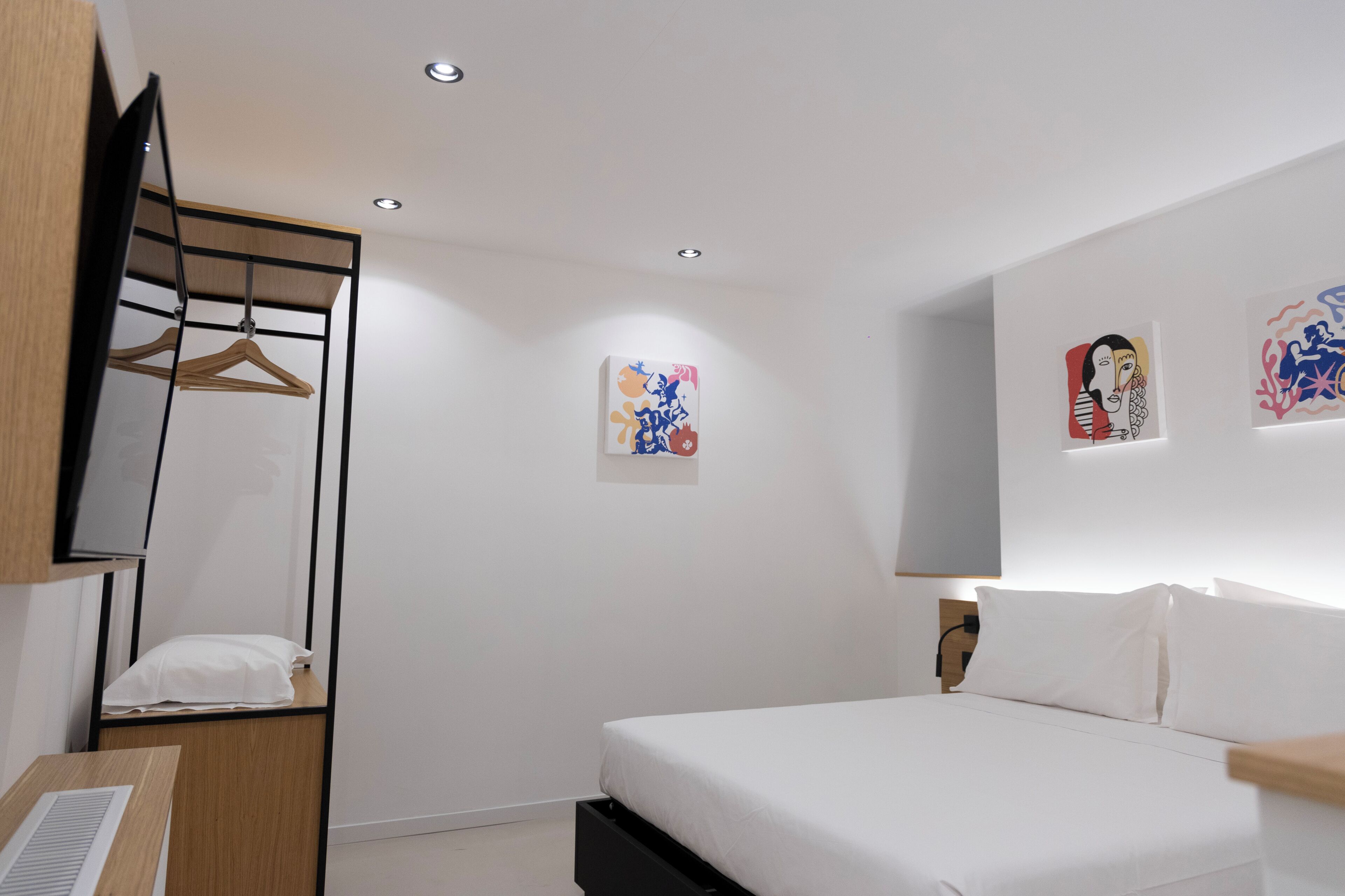 A hotel room with a bed, a desk with a computer, a mirror, and artwork on the walls.