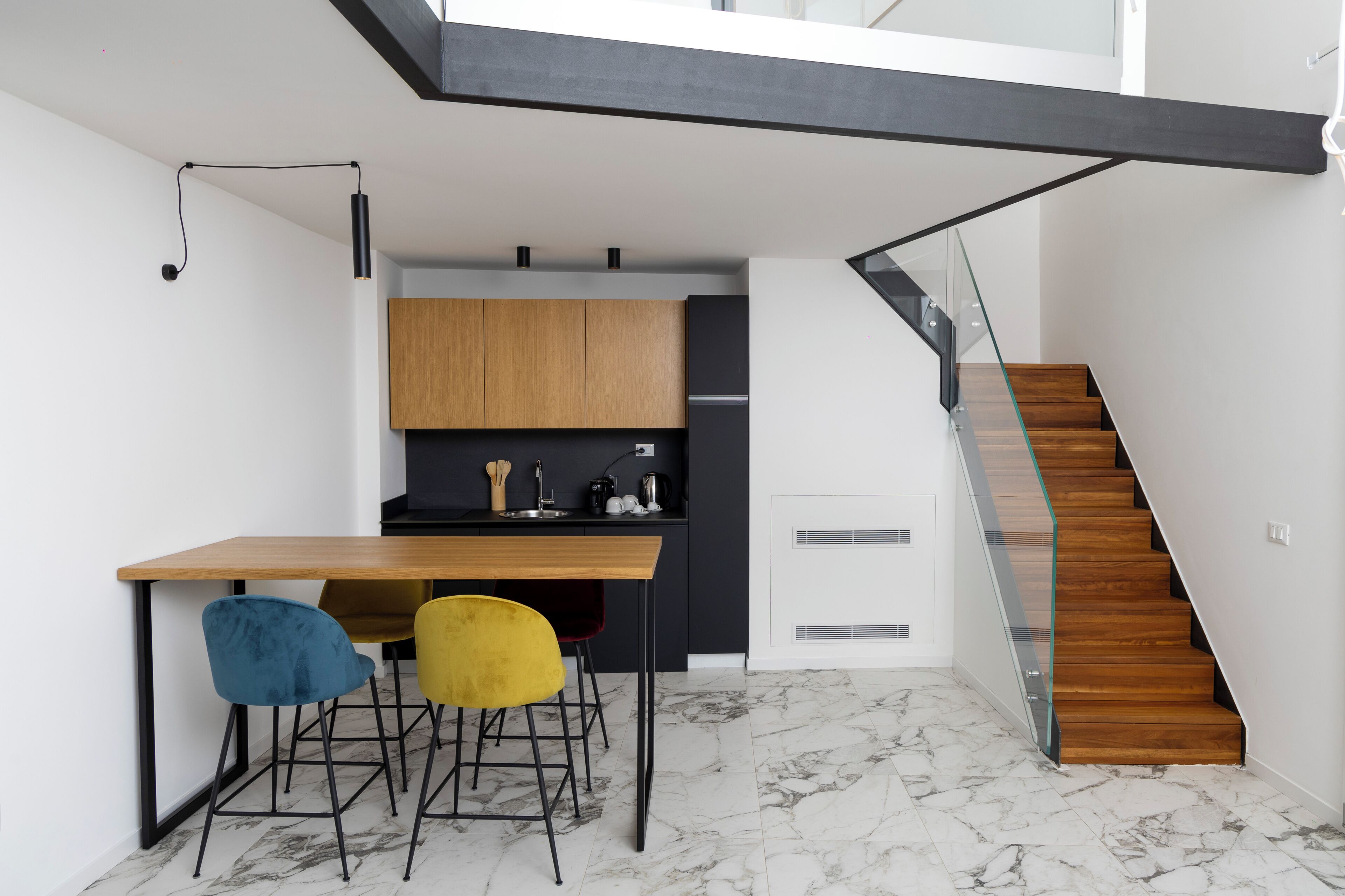 Uma cozinha moderna com mesa de madeira e duas cadeiras, escada com guarda-corpo de vidro e piso de mármore.