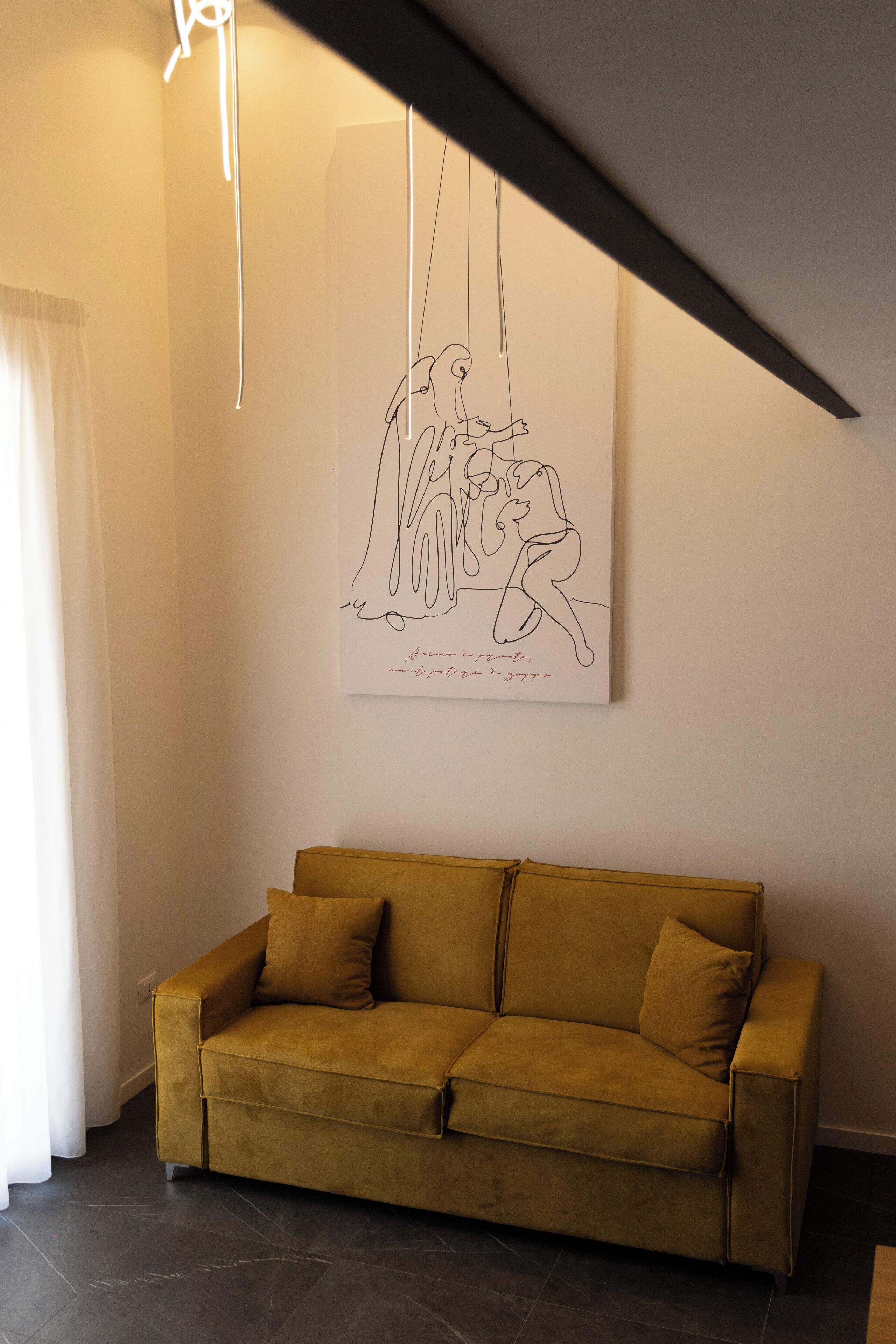 Una sala de estar moderna con un sofá, una obra de arte colgada en la pared y una lámpara en el techo.